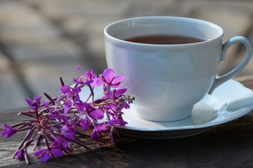 Cup of tea and flowers of fireweed on a saucer on a wooden table close-up.