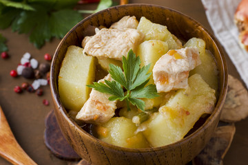 Potatoes stewed with chicken and vegetables in a wooden bowl.