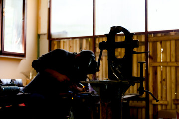 Mechanical hand vise with parallel jaws in the metalwork, craftsman welding in background
