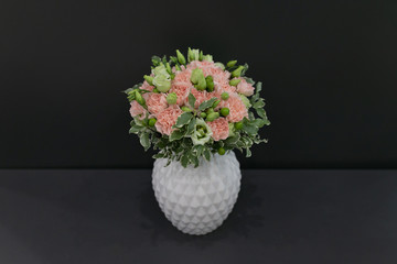 Bouquet of pink carnations and white eustoma in a snow-white vase on a dark gray background