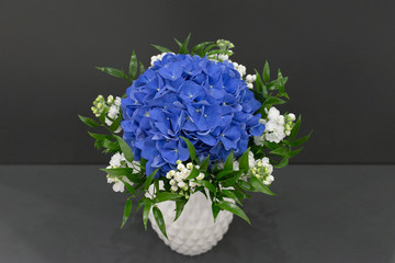 Bouquet of blue hydrangea and white flowers in a snow-white vase on a gray background