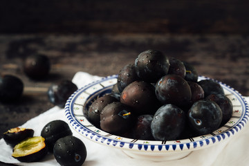 Fresh and ripe plums on a plate on a wooden background, macro, selective focus