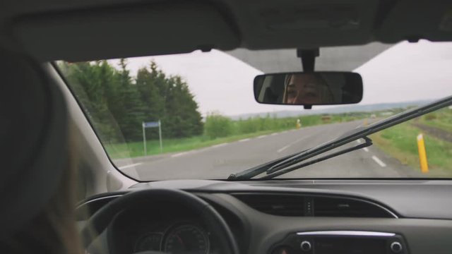 Young woman drives a car in rainy day, back view with reflection in back mirror of car, cinematic shot