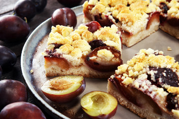 Rustic plum cake on wooden background with plums around.