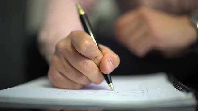 A clip of a man taking notes on a piece of paper in slow-motion CLOSE UP from the FRONT.