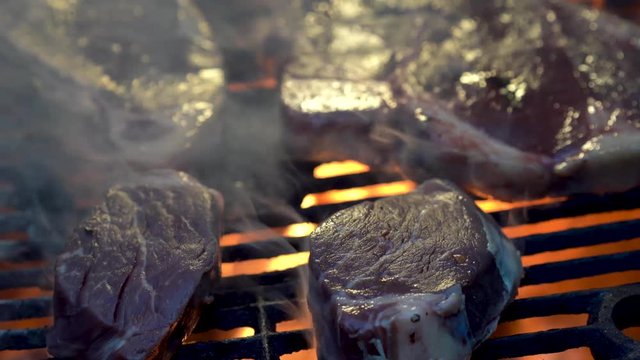 Sliding to left two choice cuts of filet mignon on a hot grill with red coals and fire cooking.