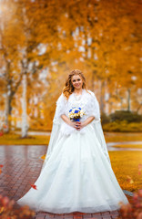 Obraz na płótnie Canvas Charming bride holding bouquet of flowers, in an autumn park