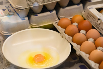 Fresh raw egg in bowl with brown eggs in carton