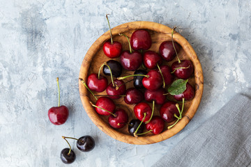 Fresh cherries on olive wood plate on gray stone background  top view