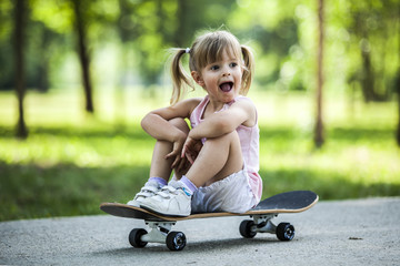 Little blonde girl playing with skateboard in forest park