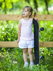 Little blonde girl playing with skateboard in forest park