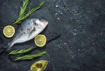 Raw fresh dorado with lemon on dark stone background. Top view