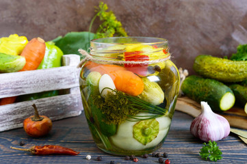 Marinated vegetables in a glass jar. Assorted cucumbers, peppers, carrots, patissons, zucchini. Pickles.