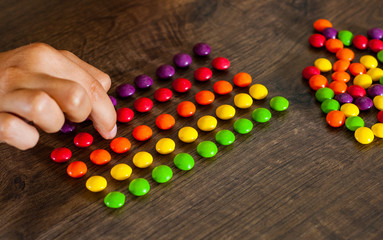 woman's hand collects even row of colorful candies on a wooden background