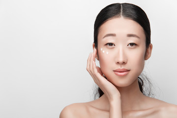 Close up beauty portrait of beautiful asian half naked woman applying face cream isolated on white...