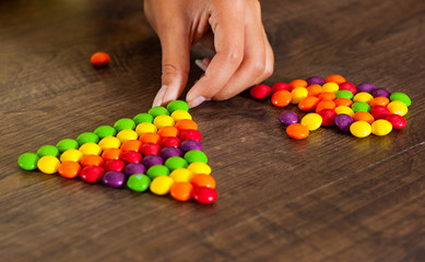 woman's hand collects even row of colorful candies on a wooden background
