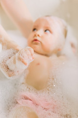 Happy laughing baby taking a bath playing with foam bubbles. Little child in a bathtub. Infant washing and bathing.