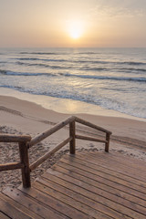 Fototapeta na wymiar Path to the beach. Sunrise at background, golden sky. Mediterranean sea (Guardamar del Segura, Spain). Vertical composition. 