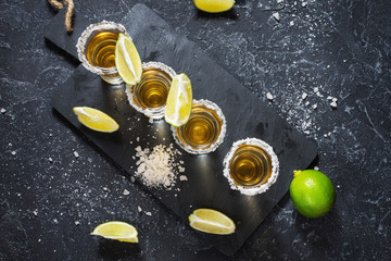 Mexican gold tequila with lime and salt on black stone background
