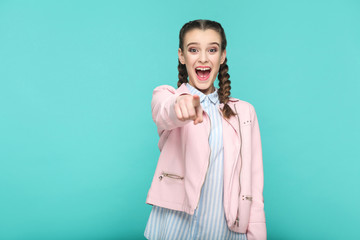 wow, amazed portrait of beautiful cute girl standing with makeup and brown pigtail hairstyle in striped light blue shirt pink jacket. indoor, studio shot isolated on blue or green background.