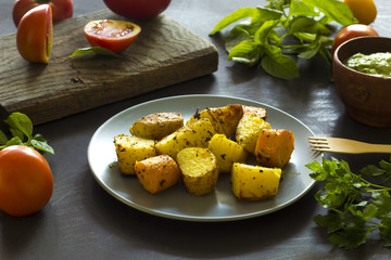 Baked potatoes, greenery sauce, fresh tomatoes, basil leaves and parsley on the kitchen table. 