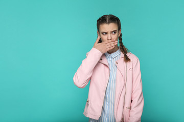 I'm silent. portrait of beautiful cute girl standing with makeup and brown pigtail hairstyle in striped light blue shirt pink jacket. indoor, studio shot isolated on blue or green background.