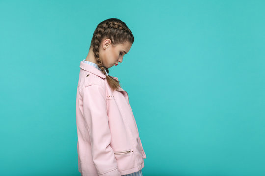 profile side view of sad unhappy depressed portrait of beautiful cute girl standing with makeup and brown pigtail hairstyle in pink jacket. indoor, studio shot isolated on blue or green background.