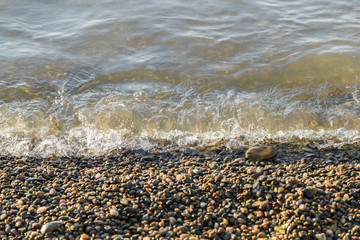 Fototapeta na wymiar pebbles on the beach pebbles on the sea shore and waves of water illuminated by the rays of the sun.