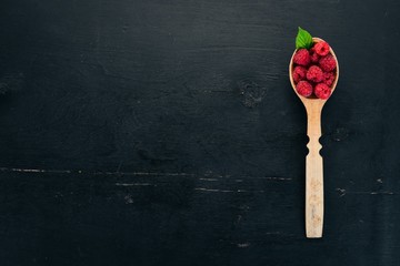 Fototapeta na wymiar Raspberry berries in a wooden spoon. On a wooden background. Top view. Free space for your text.
