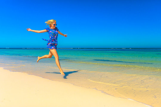 Beach freedom summer vacation. Joyful happy woman jumping on seashore of white sand in popolar Hangover Bay, Cervantes, Nambung National Park, Western Australia. Blonde girl happiness jump. Copy Space