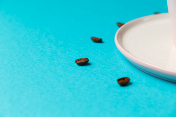 Coffee cup with spoon on saucer and coffee beans against blue background forming clock dial. Coffee as symbol of morning energy and cheerfulness or evening refreshment. Close up. Concept