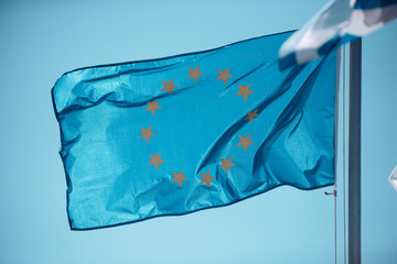 Flag of european union flying on background of blue sky. Symbol of unity of Europe. Circle of 12 gold stars on blue background.