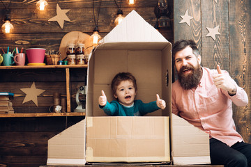 happy kid sit in cardboard hand made rocket. Parenthood concept. Boy play with dad or father,...