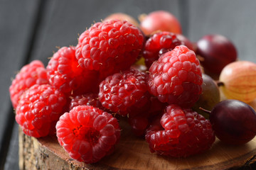 Ripe organic berries. Heap of raspberries and gooseberries on wood slab