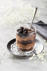 Chocolate layered dessert in a  glass with blackberries on grey background