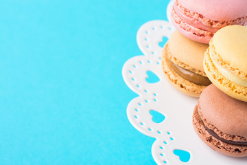 Variety of Multicolored Pink Green Yellow Brown Mocha Coffee Macarons Stacked on White Lace Cake Stand on Turquoise Background. Bakery Confectionery Pastry Shop Poster Banner Template. Party Wedding