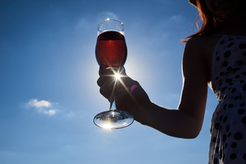 girl holds the glass of wine on her hand with sky background