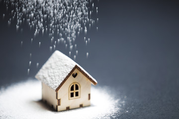 Wooden decorative toy house standing in winter undedr snow on black background. Purchasing or buying a house or rental of property, cosy home and new house for children concept