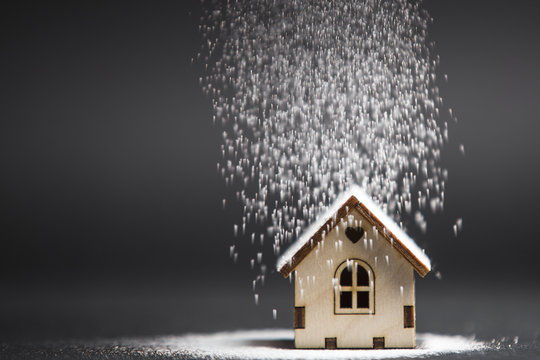 Wooden Decorative Toy House Standing In Winter Blizzard On Black Background. Purchasing Or Buying A House Or Rental Of Property, Cosy Home And New House For Children Concept