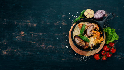 Sausages in sauce and vegetables in a frying pan. On a wooden table. Top view. Copy space.