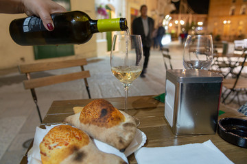 Street food in South Italy, waiter pouring cold white wine in glass, table with two pizza...