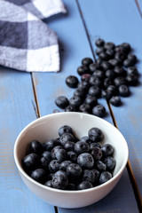 White bowl full of blueberry on a blue wooden table with a blue and white checkered dish towel