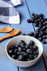 White bowl full of blueberry on a blue wooden table with a blue and white checkered dish towel