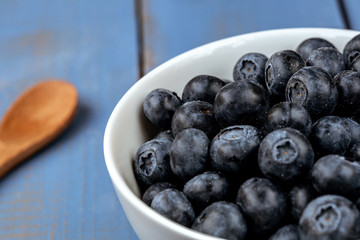 Macro photography of a white bowl full of blueberry on a blue wooden table
