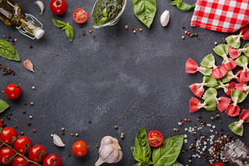 Italian flag farfalle pasta on dark background with copy space horizontal. Cherry tomatoes, garlic, basil, pesto, olive oil, pepper mix, salt and red napkin