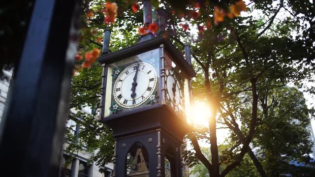 Sun shines through the trees behind the steam clock in Gastown, Vancouver, at dawn, circling pan
