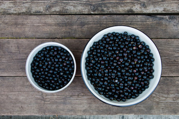 Beautiful natural black berries in asmall and large bowls on wooden background top view
