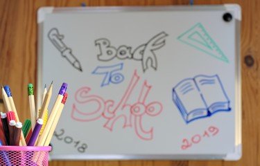 White board with illustration back to school and close-up container with school supplies.Photo with blurred background.