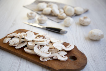 Fototapeta na wymiar Chopped mushrooms on rustic wooden chopping board, closeup. White wooden background. Side view.