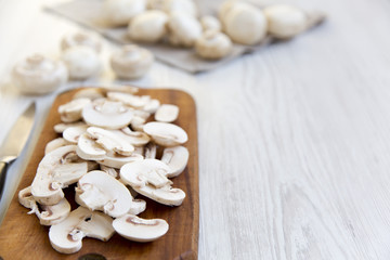 Chopped mushrooms on wooden chopping board over white wooden background, close-up. Side view. Copy space.